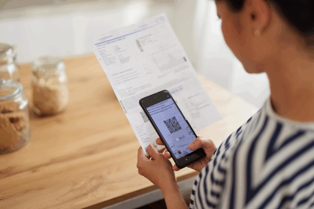 Woman standing in kitchen paying bills with phone onliine